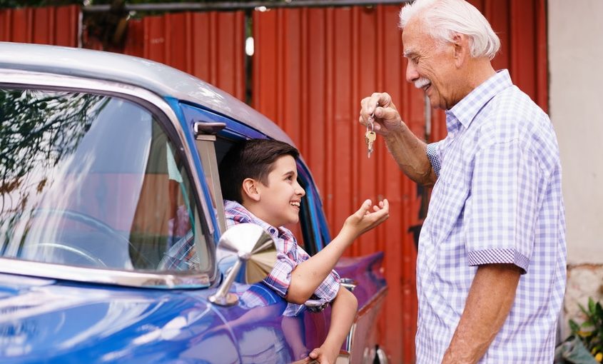 Opa überreicht seinem im Auto sitzenden Enkel die Autoschlüssel