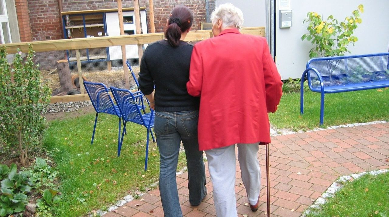 Oma mit Stock bei jüngerer Frau am Arm gestützt