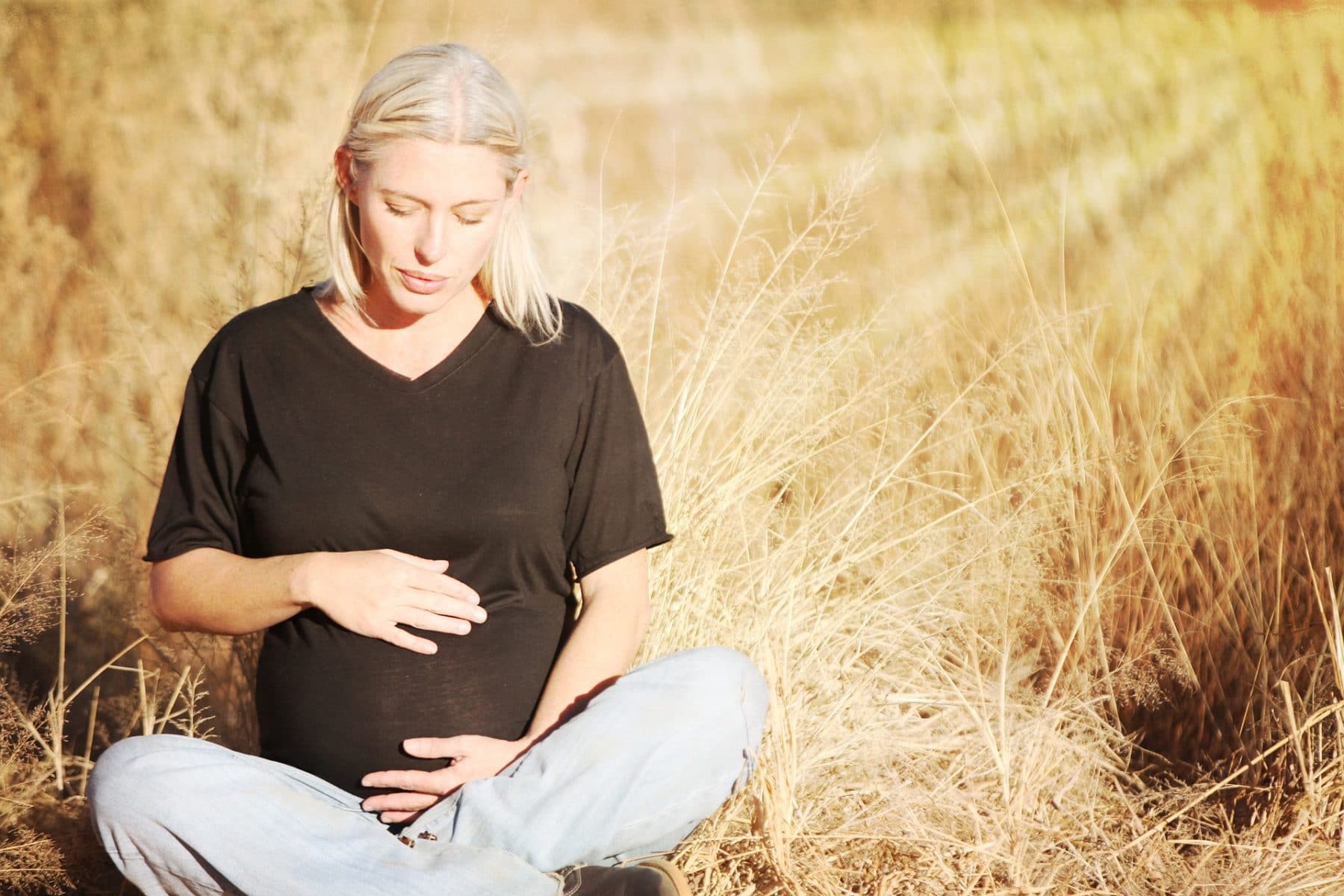 Schwangere Frau im Schneidersitz auf einem Kornfeld